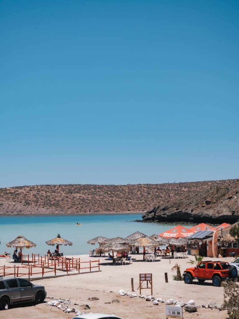 затінені зони відпочинку та кілька автомобілів, припаркованих на Playa El Tesoro в La Paz Baja