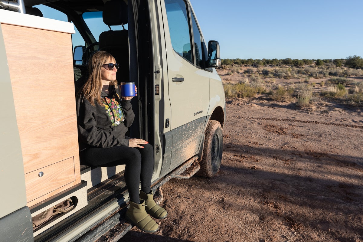 Засновник Bearfoot Theory Крістен Бор сидить на краю Sprinter Van і п’є каву в Моабі.