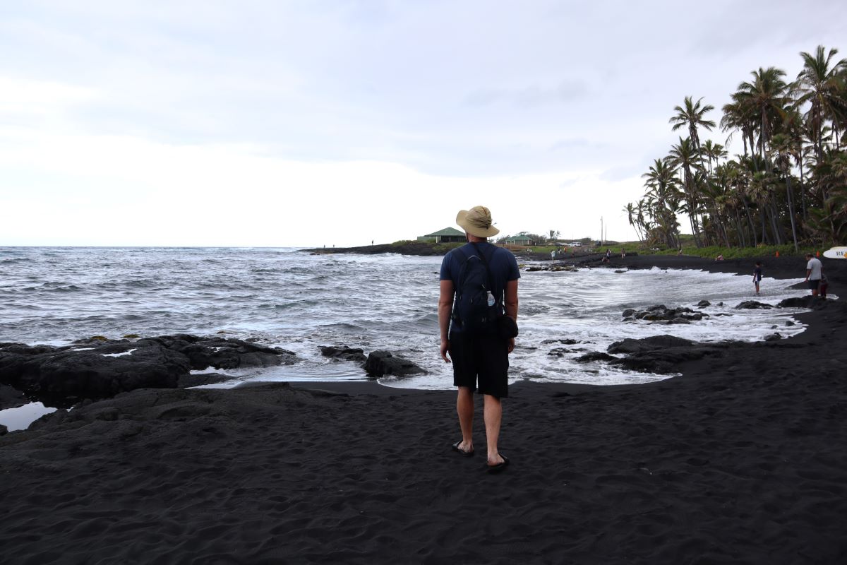Чоловік стоїть на пляжі Пуналу'у з чорним піском на Гаваях