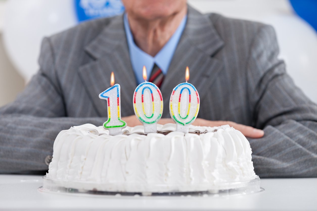 muž v obleku před narozeninovým dortem se svíčkami číslo 100